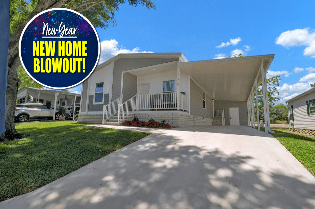 Single-story manufactured home with front porch, covered driveway, and landscaped yard under a blue sky. A circular graphic at top left reads "New Year NEW HOME BLOWOUT!.