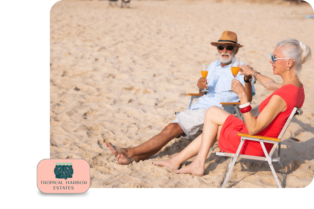 An older man and woman sit on beach chairs in the sand, holding orange drinks and talking. The Tropical Harbor Estates logo appears in the bottom left corner.