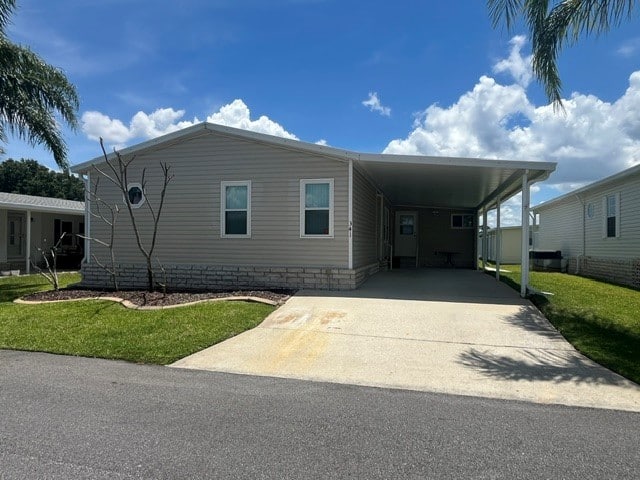 Single-story beige manufactured home with carport, driveway, small lawn, and partly cloudy sky.